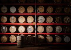 Trähyllor med staplade ekfat i ett lagerutrymme, en ensam tunna står framför hyllorna.