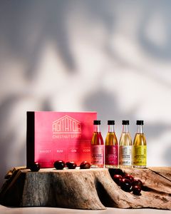 Fyra små flaskor sprit med olika färger står bredvid en röd låda märkt "Agitator Chestnut Spirits" på en träyta.