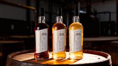 Tre flaskor med whisky står på en trätunna i ett svagt upplyst rum.