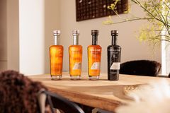 Fyra whiskyflaskor på ett träbord. Tre är gyllene och en är svart.