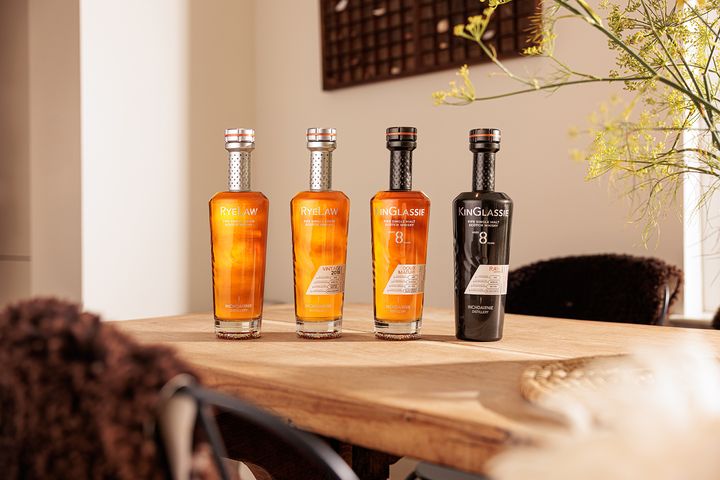 Fyra whiskyflaskor på ett träbord. Tre är gyllene och en är svart.