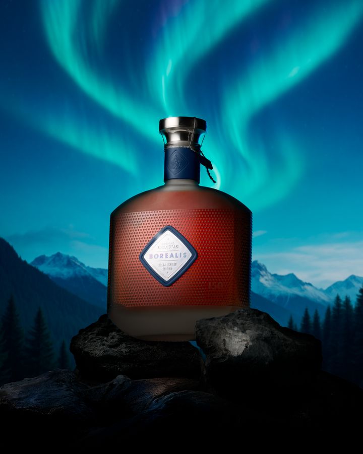 Flaska cognac placerad mot en bakgrund av norrsken och bergslandskap.