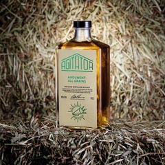 Flaska med "Agitator Argument: All Grains" whisky placerad framför hö.