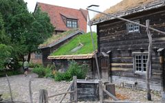 En man går på en stenlagd väg bredvid Blekingegården, en historisk byggnad med grästak, på Kulturen i Lund.