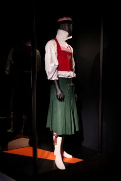 Mannekäng med en könsinkluderande skånsk folkdräkt i rött och grönt.