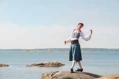 En person i folkdräkt står på en klippa vid havet