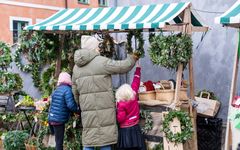 Personer handlar julkransar från ett marknadsstånd dekorerat med gröna kransar.