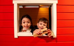 Två barn leker i ett fönster på en röd lekstuga.