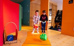 Två barn kastar stora tärningar på en bana i ett lekutställningsområde.