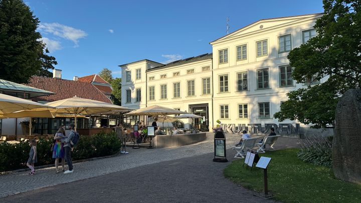 Bild av Kulturens Vita huset, en historisk byggnad från 1850-talet. Framför byggnaden finns parasoller och människor som går omkring.