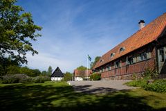 Bild på en korsvirkesbyggnad med svenska flaggan utanför, omgiven av grönska under en blå himmel.