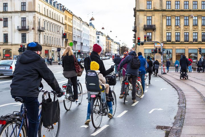 Cykelpendlare i Köpenhamn på en cykelbana omgivna av äldre byggnader.