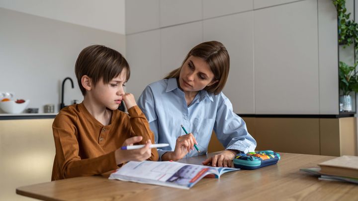 En vuxen hjälper ett barn med läxor vid ett bord i hemmet.