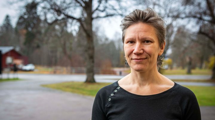 Kristina Palm Kaplan framför en landskapsbakgrund med träd och en väg.
