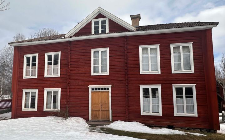 Rött trähus med vita fönsterkarmar, Erik-Andersgården i Hälsingland. Snö på marken.