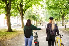 Två kvinnor leder cyklar i en park.