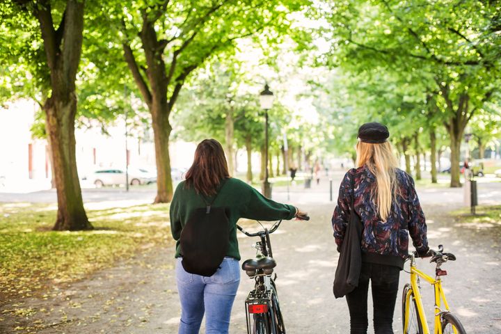Två kvinnor leder cyklar i en park.