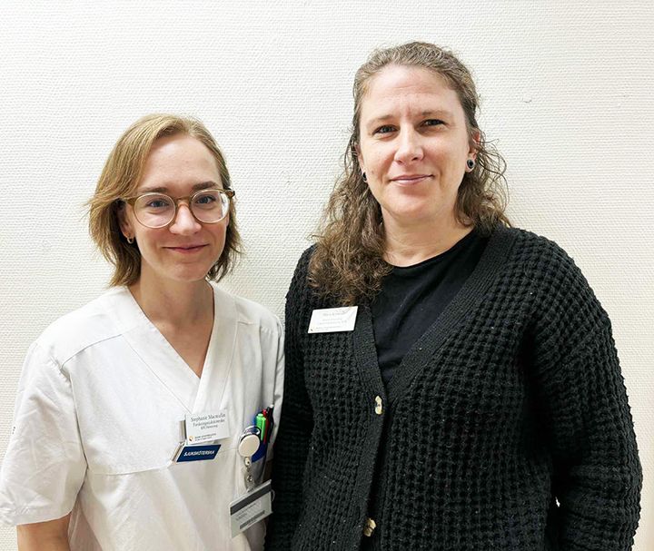 Två personer står bredvid varandra, en i vit sjukhusrock och den andra i svart tröja.