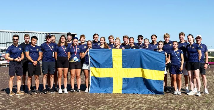 En grupp unga personer i blå tröjor står tillsammans och håller upp en svensk flagga.