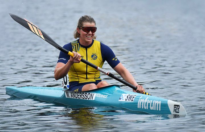 Kvinna paddlar en kajak på vattnet, iklädd gul och blå sportklädsel.