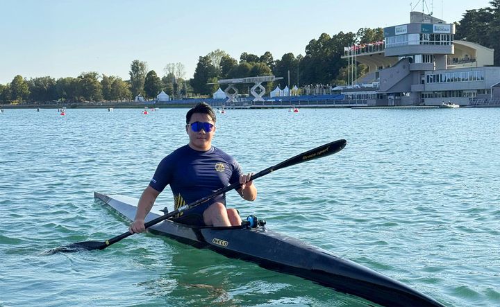 En person paddlar kajak på en sjö med en byggnad i bakgrunden.