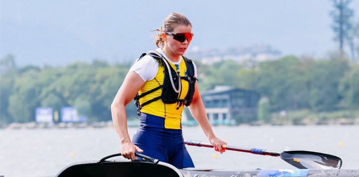 Kvinna i gul och blå dräkt paddlar under en tävling.