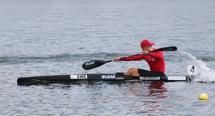 Person paddlar snabb kajak på vattnet, iklädd röd tröja och mössa.