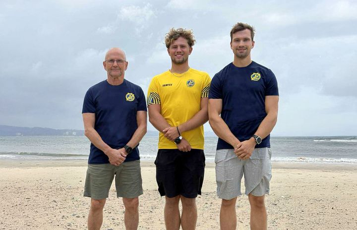 Tre personer från den svenska truppen står på en strand i träningskläder.