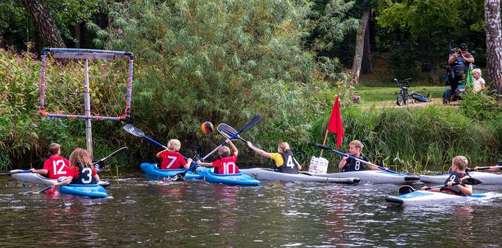 Alt text: Flera barn spelar kanotpolo i en flod.