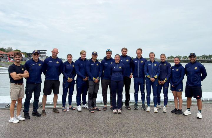 Gruppfoto av svenska sprintlandslaget i Szeged. Flera personer i blåa träningskläder står vid en kaj, två saknas.