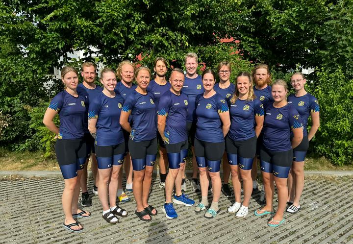 Gruppfoto av den svenska idrottstruppen i blå träningskläder, utomhus framför träd i München.