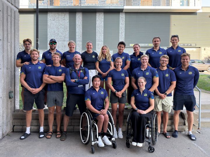En grupp människor i lagkläder, inklusive två personer i rullstol, står utomhus för ett foto.