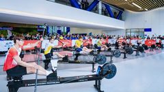 Deltagare tävlar på kajakergometer i en inomhusarena med publik.