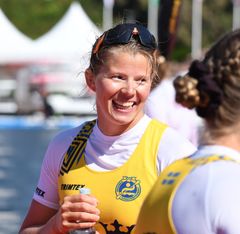 Melina Andersson leende i gul tävlingströja utomhus, med en annan person synlig i förgrunden.