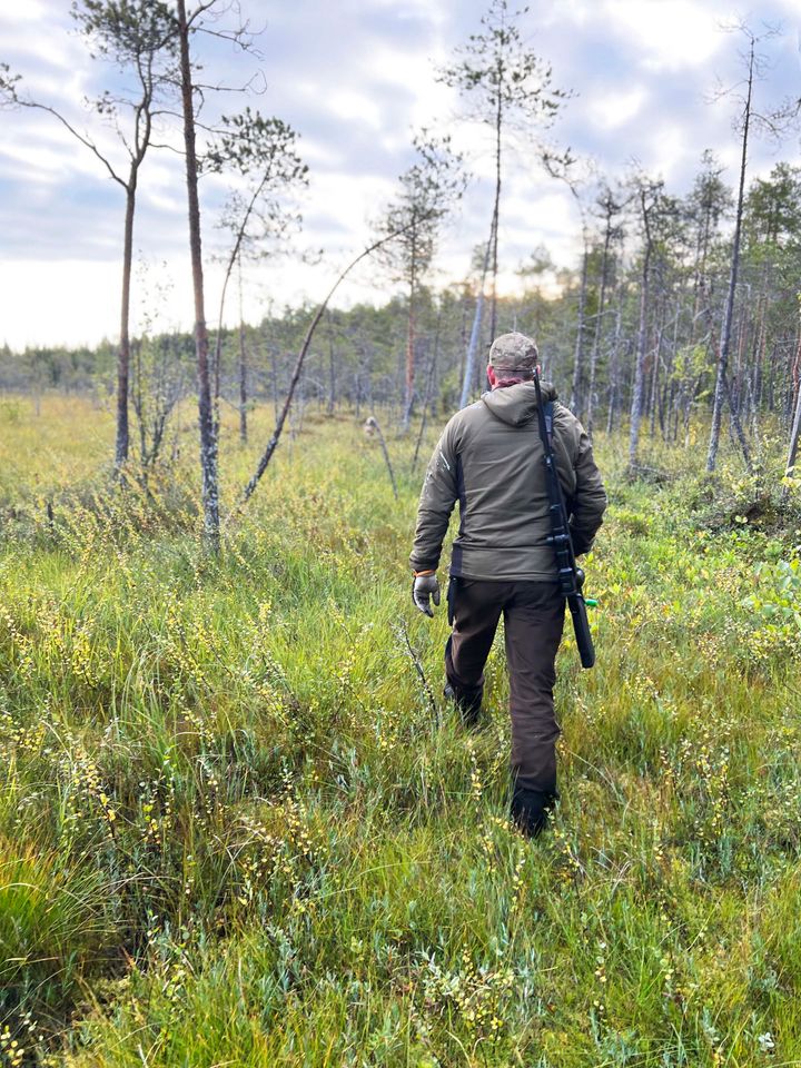 Person som går genom en skogsklädd äng iklädd jaktkläder.