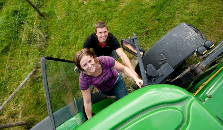 Kvinna och man klättrar upp i grön traktor