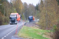 Landsväg med två lastbilar som kör i motsatt riktning. Skog i bakgrunden.