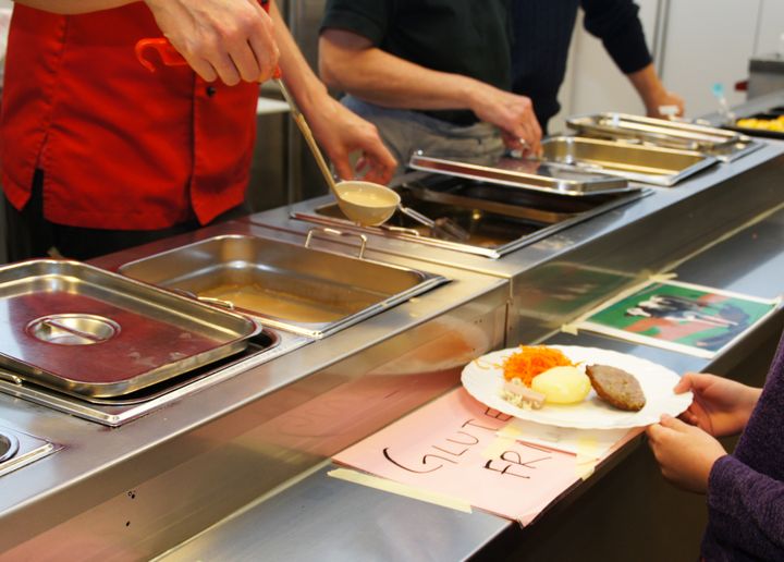 Person serverar mat på en tallrik vid en buffé.