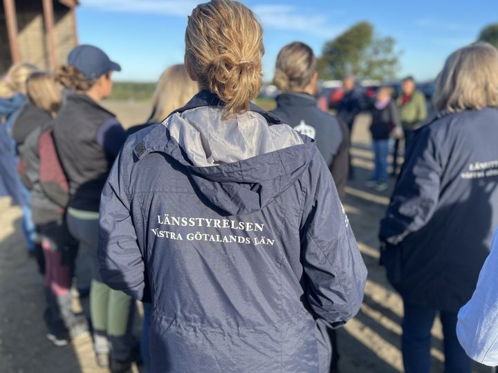 En grupp människor står utomhus. En person har en jacka med texten "Länsstyrelsen Västra Götalands län" på ryggen.
