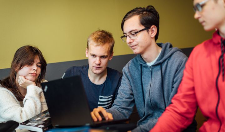 Fyra personer sitter vid ett bord och tittar på en bärbar dator tillsammans.