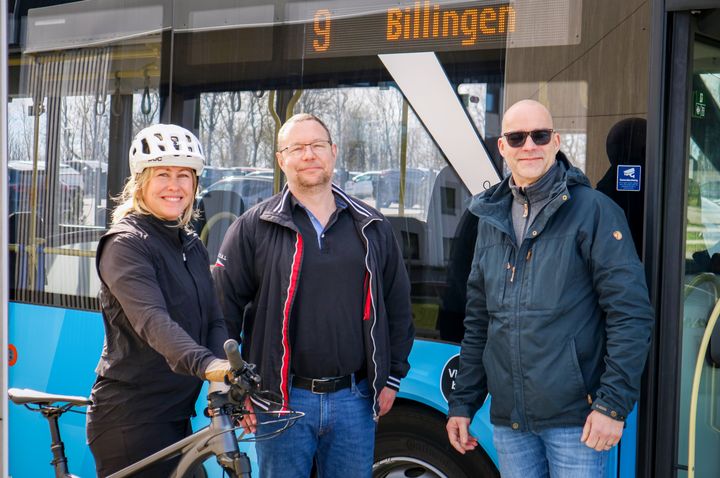 Tre personer, varav en med en cykel, står framför en buss.