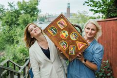 Jag kan inte identifiera personerna på bilden, men här är ett förslag till alternativ text: Två kvinnor håller tillsammans i en resväska dekorerad med klistermärken, omgivna av grönska och träbyggnader.