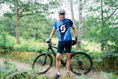 En man i cykelkläder står med sin cykel i en lummig skogsmiljö.