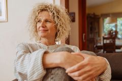 En kvinna med lockigt hår sitter avslappnat i ett hem.