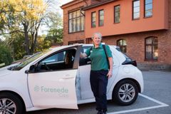 En person står bredvid en bil märkt med "Forenede Care" framför en byggnad.