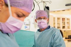 Två kirurger i operationskläder och munskydd arbetar i ett operationsrum.