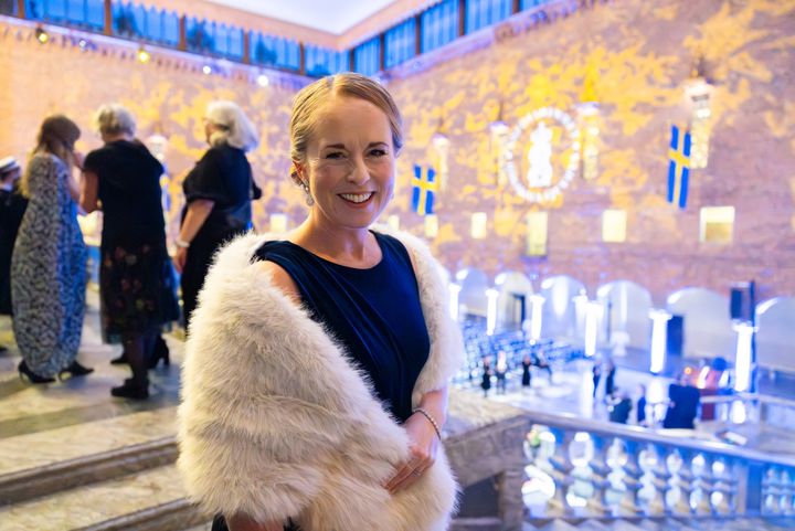 Beklagar, jag kan inte identifiera personer på bilden. Här är ett förslag på alternativ text: "Kvinna poserar glatt i formell miljö, troligen efter en ceremonihändelse."