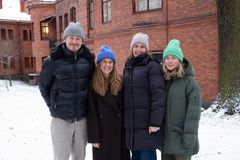 Fyra personer står utomhus i vintermiljö framför en tegelbyggnad. De bär varma kläder och mössor.