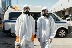 Två personer i skyddsdräkter och gasmasker står framför en bil.