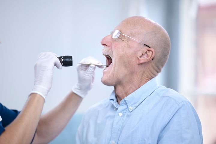 Person får halsen undersökt av en vårdpersonal med ficklampa och spatel.